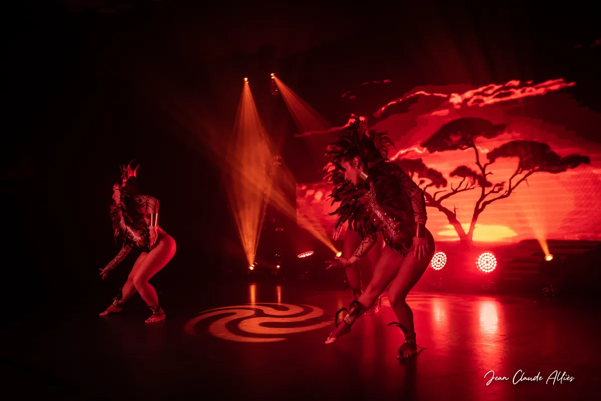 Danseuses coiffées de plumes devant un paysage de savane projeté dans une lumière rouge.
