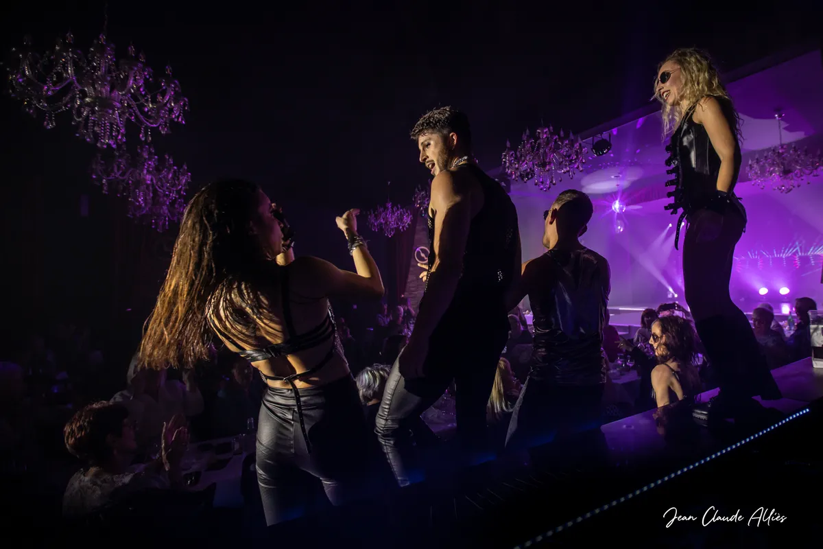 Danseuses en tenues noires et chanteur évoluant près des spectateurs sous une lumière violette.