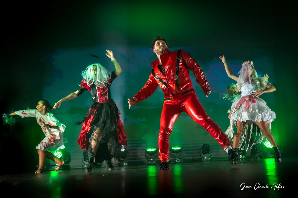 Troupe en mouvement avec un danseur en rouge au centre et des projecteurs verts en fond de scène.