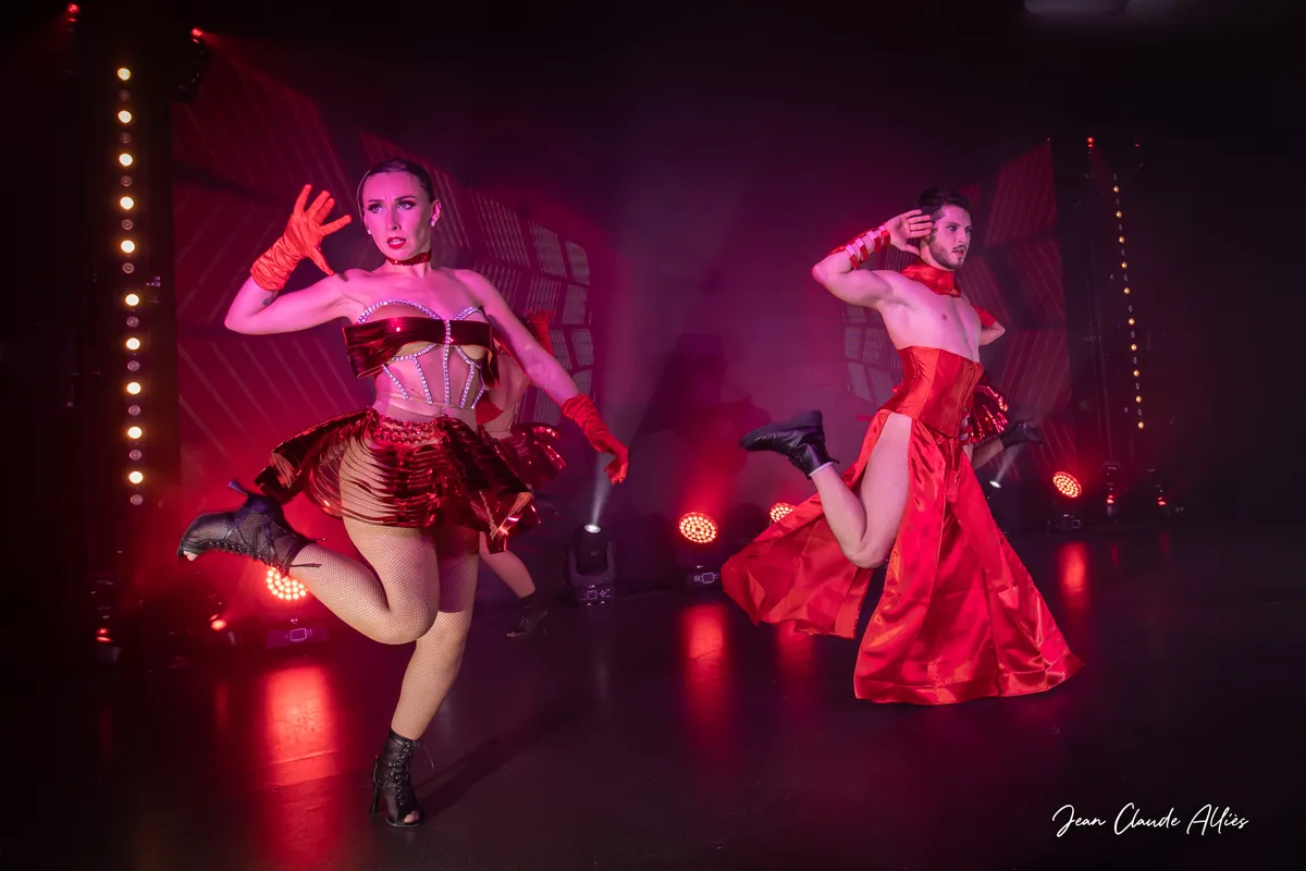 Danseuse en jupe rouge levant une jambe devant un danseur en pantalon rouge et cape assortie.