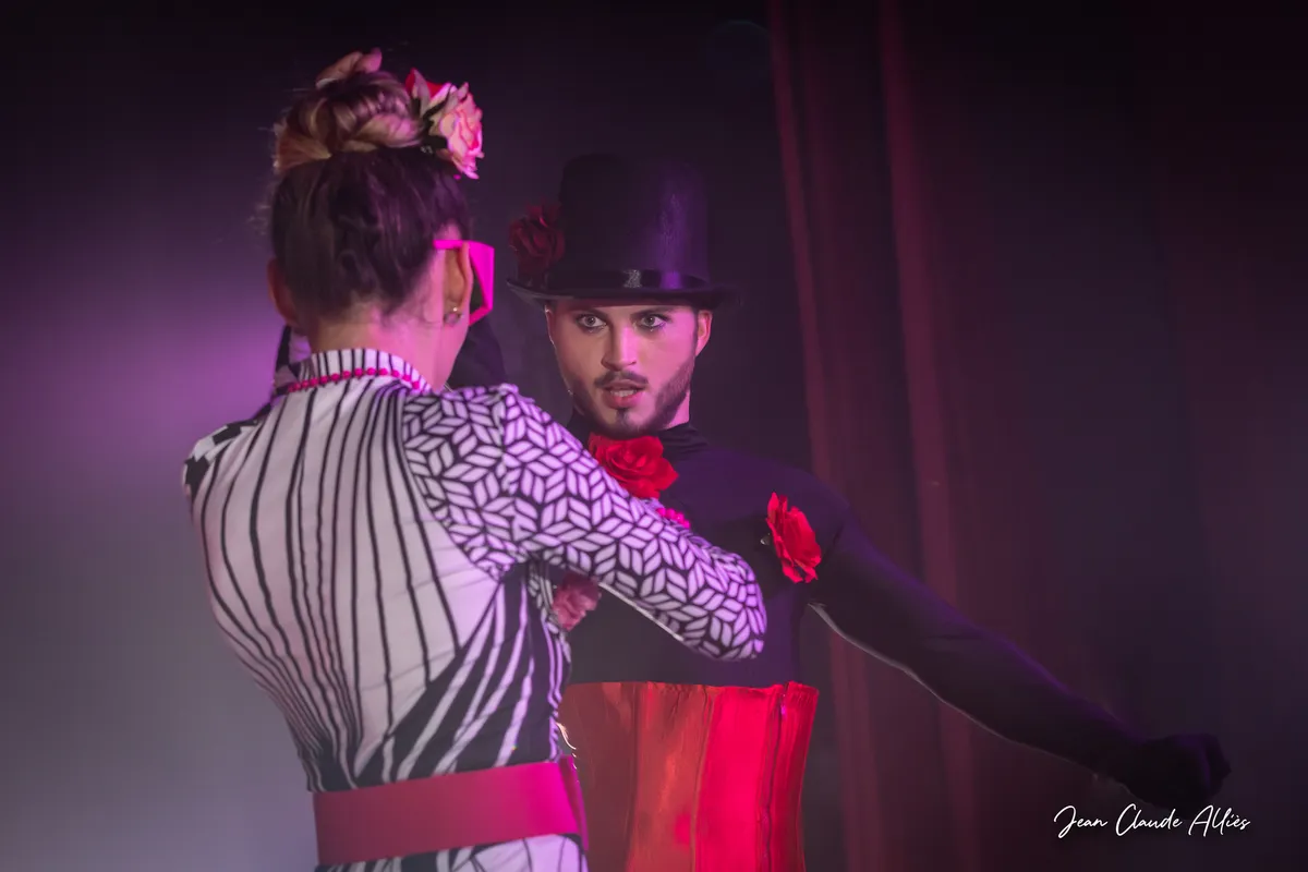 Danseuse vue de dos en costume rayé et graphique face à un danseur en chapeau noir et ceinture rouge.