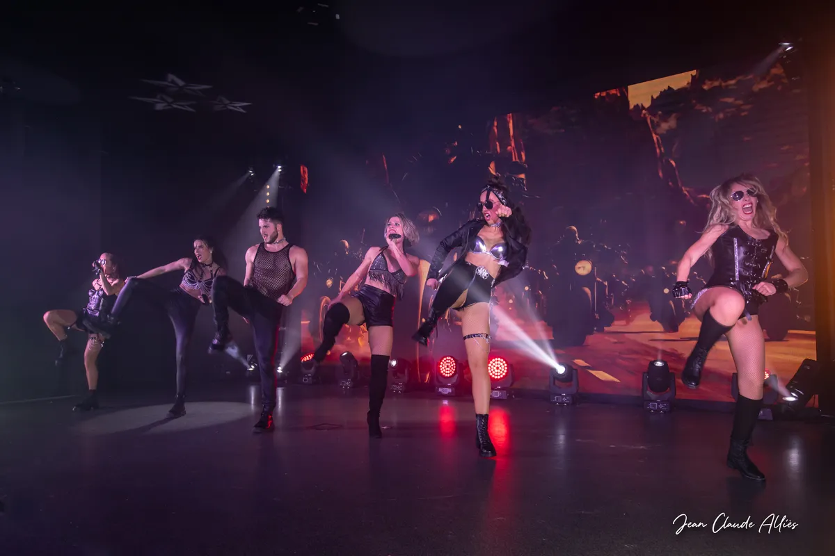 Troupe en tenues noires levant les jambes devant une projection de flammes et des projecteurs rouges.