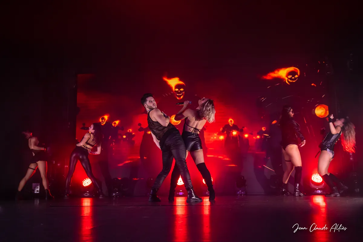 Danseur en noir et danseuse en tenue sombre au centre d'une chorégraphie éclairée en rouge.