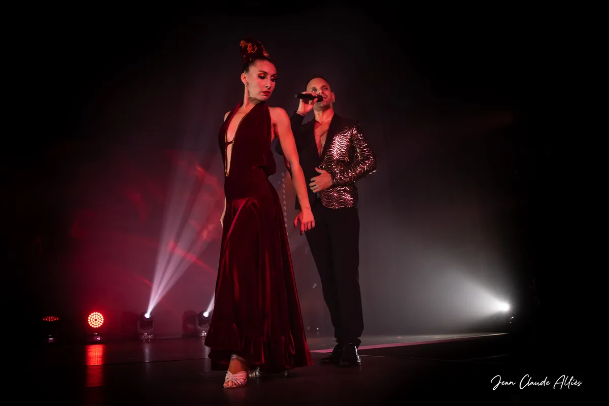 Danseuse en longue robe bordeaux devant un chanteur en chemise brillante, dans une lumière rouge.