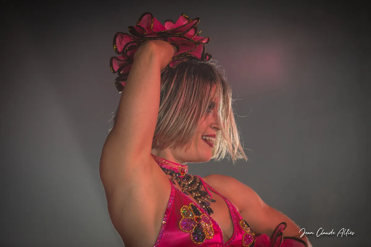 Portrait d'une artiste aux cheveux courts en costume rose et doré, un bras levé au-dessus de la tête.