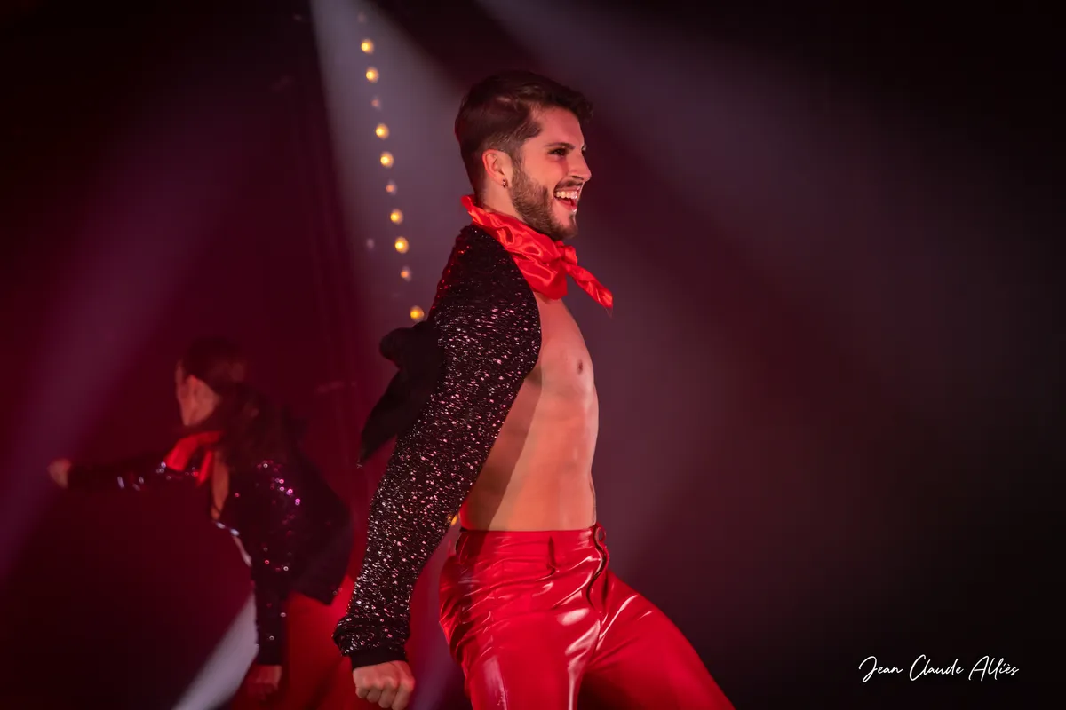Danseur souriant en pantalon rouge brillant, foulard rouge et veste noire ouverte.