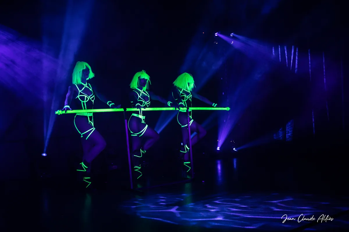 Trois silhouettes aux lignes vertes fluorescentes en mouvement derrière une barre, dans des faisceaux bleus.