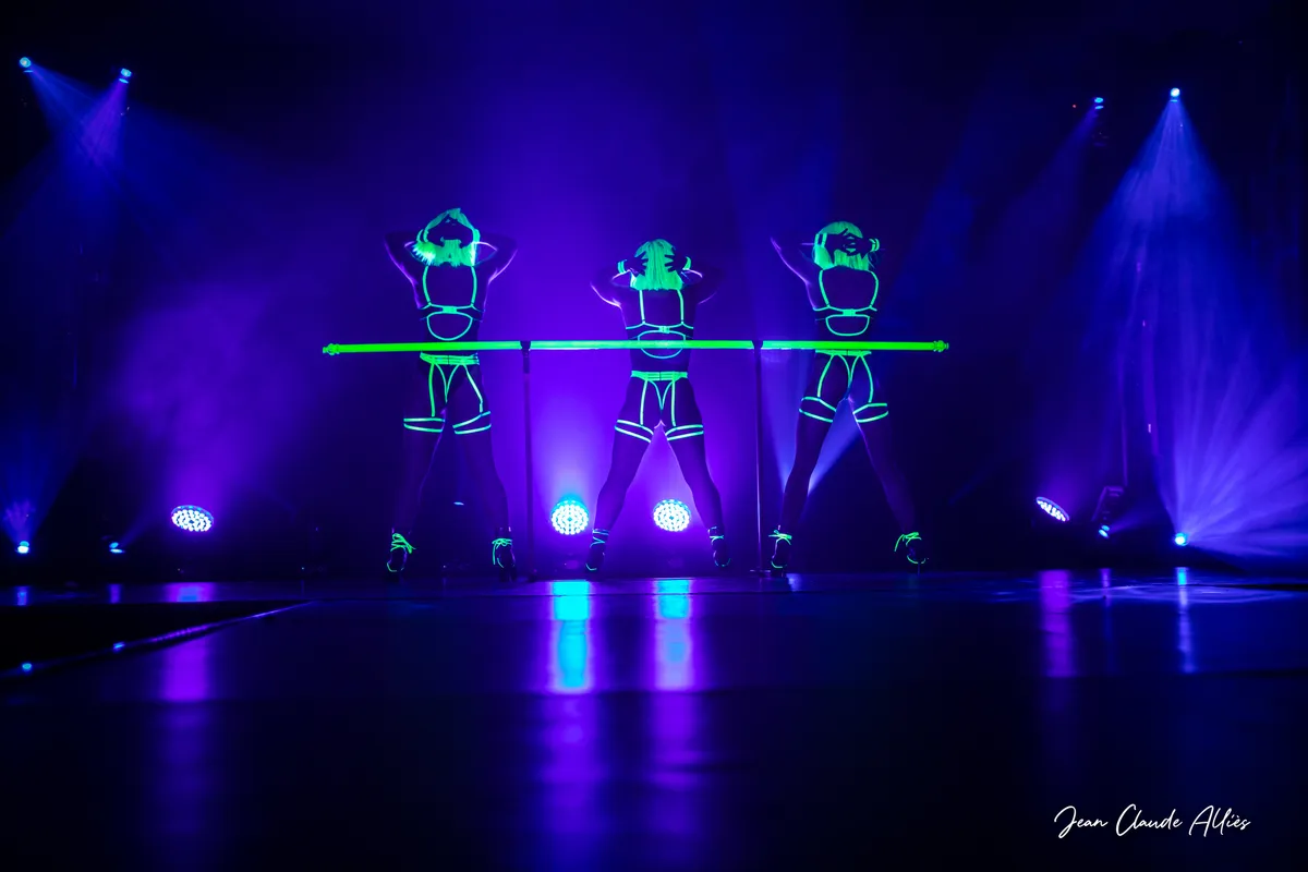 Trois danseuses en costumes fluorescents verts, les bras au-dessus de la tête, dans une lumière bleue et violette.