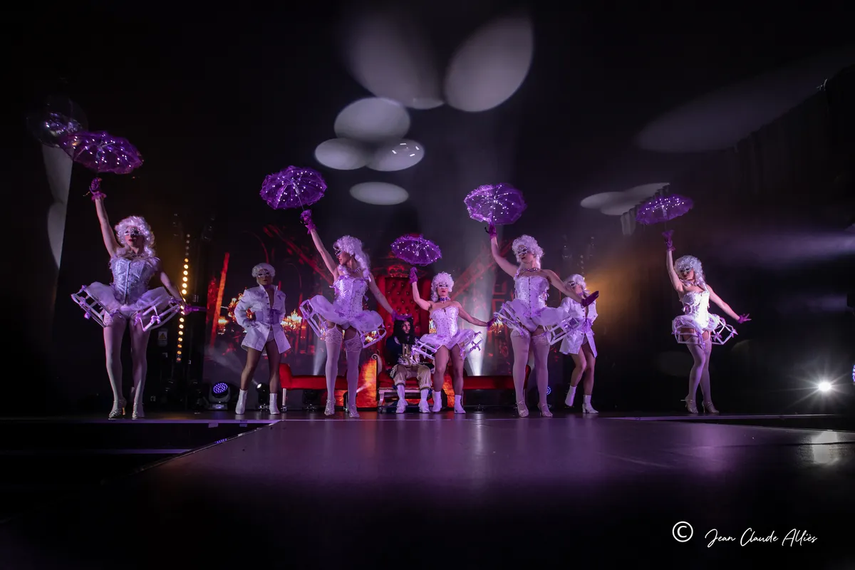 Danseuses levant leurs ombrelles violettes autour d'un trône rouge sous des motifs lumineux blancs.