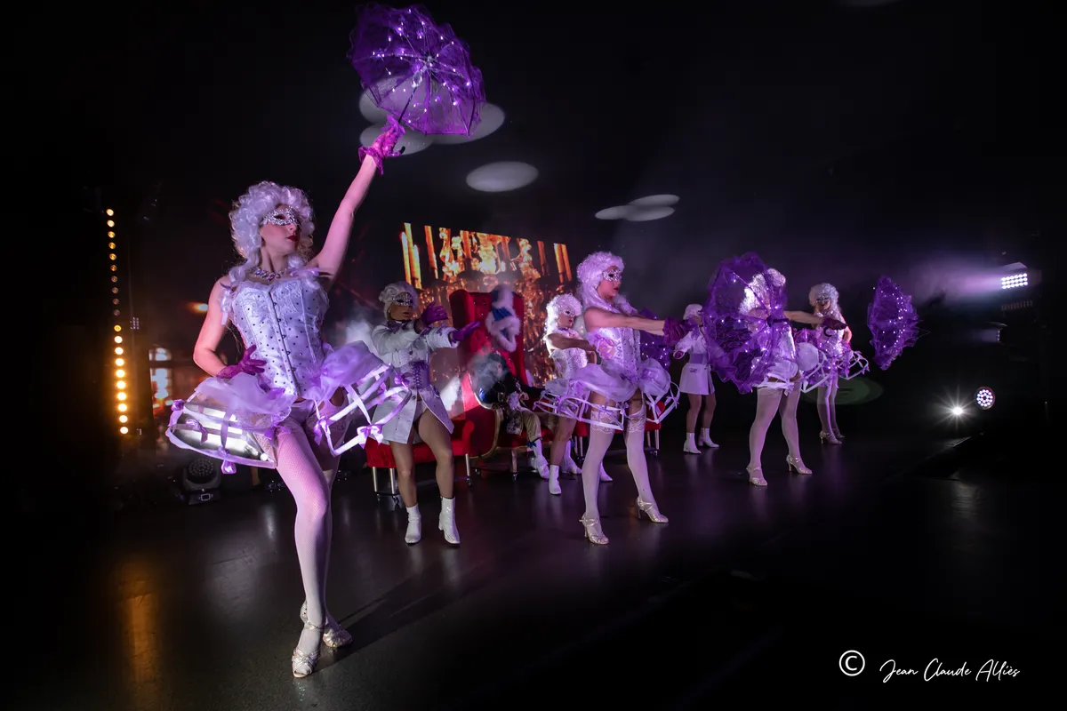 Danseuse en perruque blanche brandissant une ombrelle violette devant une ligne de costumes de cour argentés.