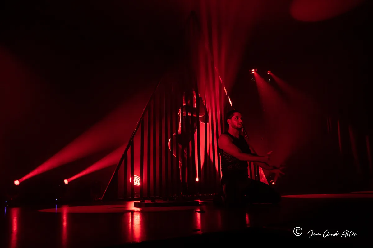Danseuses prenant appui sur un décor de barreaux verticaux au milieu de faisceaux rouges.