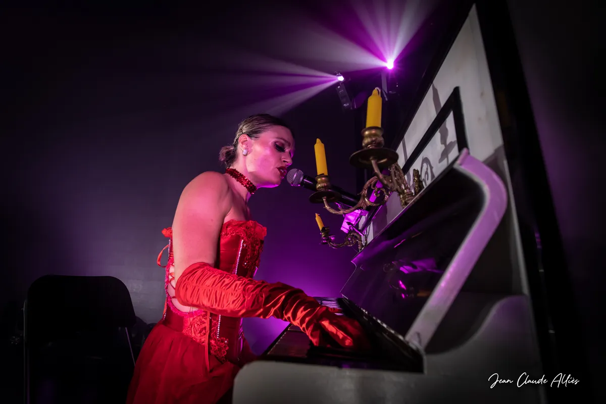 Chanteuse en tenue rouge jouant au clavier devant un microphone sous les projecteurs violets.