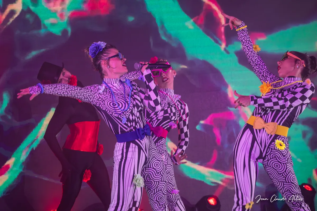 Danseuses en costumes graphiques ouvrant les bras devant une projection de couleurs vives.